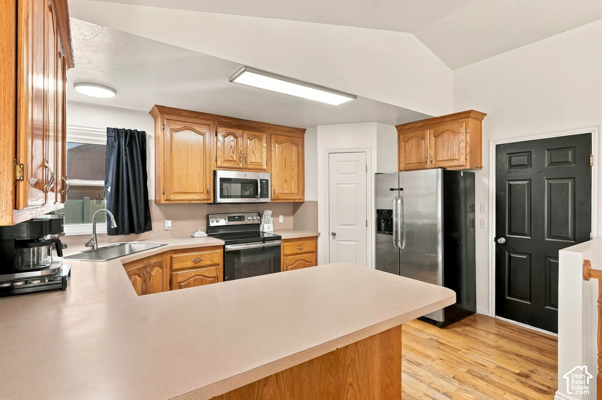 Kitchen featuring wood-finish cabinetry, stainless steel appliances, a double basin sink, and a light-toned countertop