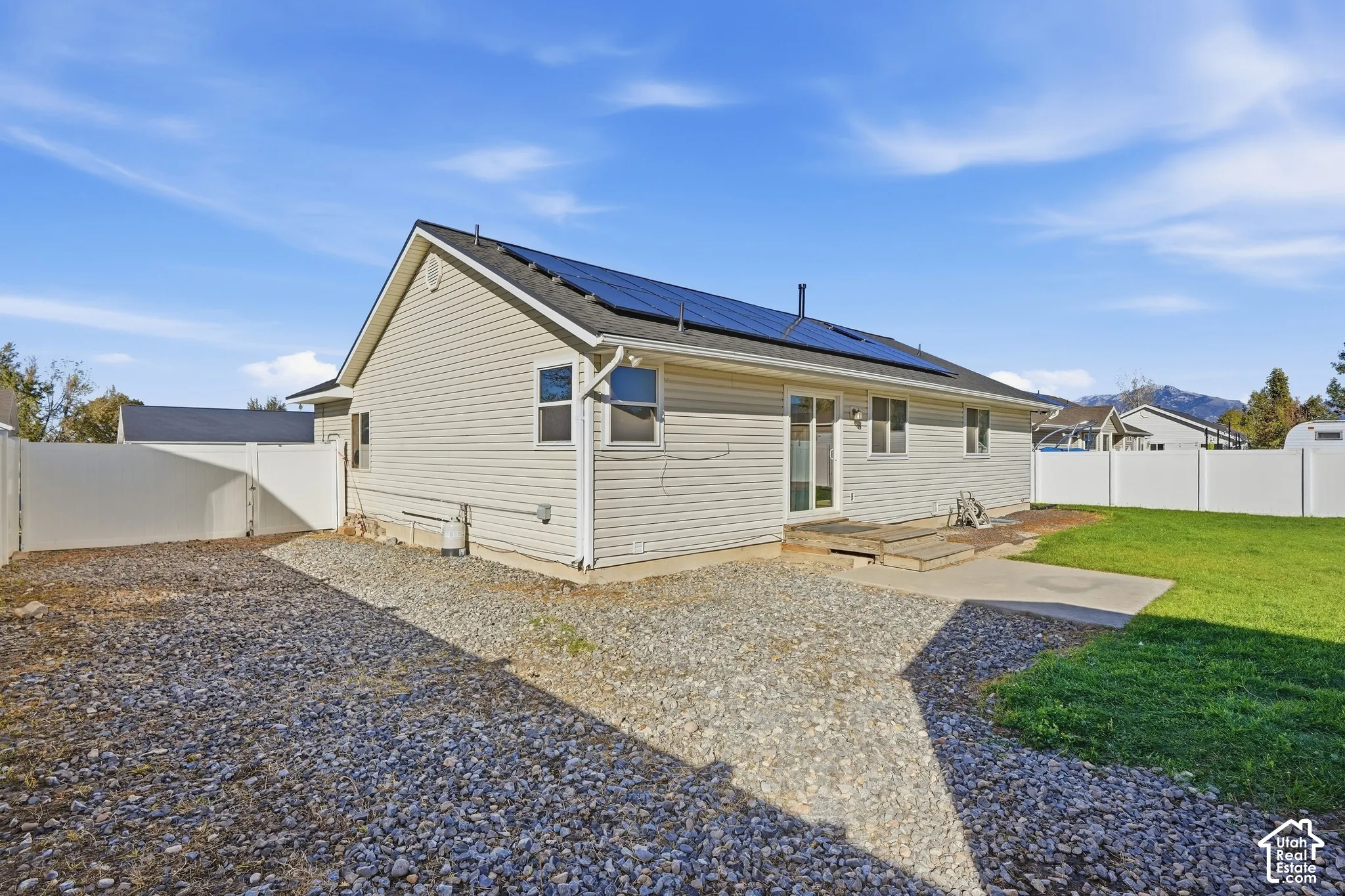 Rear exterior featuring light-toned siding, dark roof shingles with solar panels, and a concrete patio