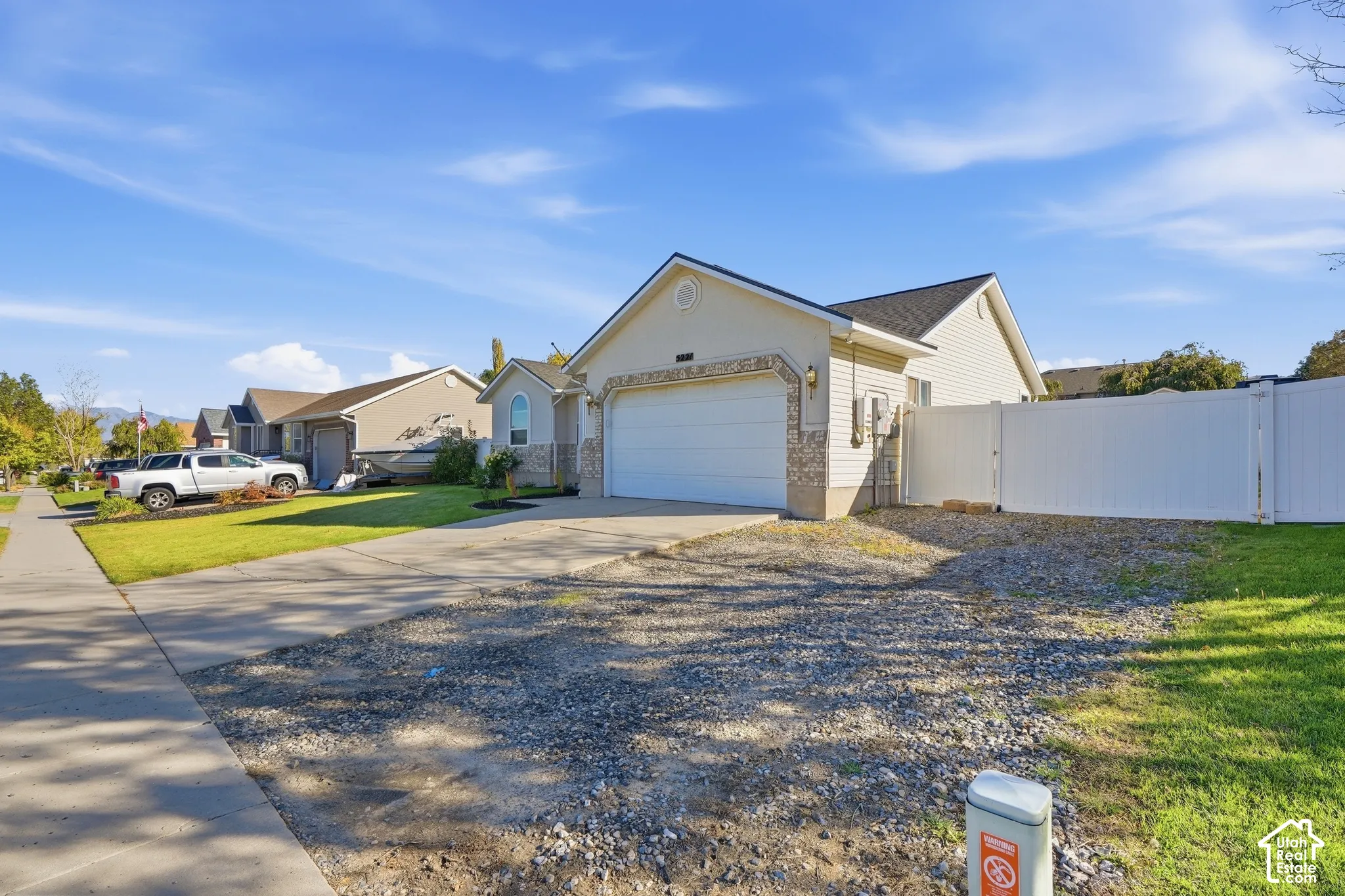Single-story residence featuring a two-car garage, stone facade accents, and a white privacy fence