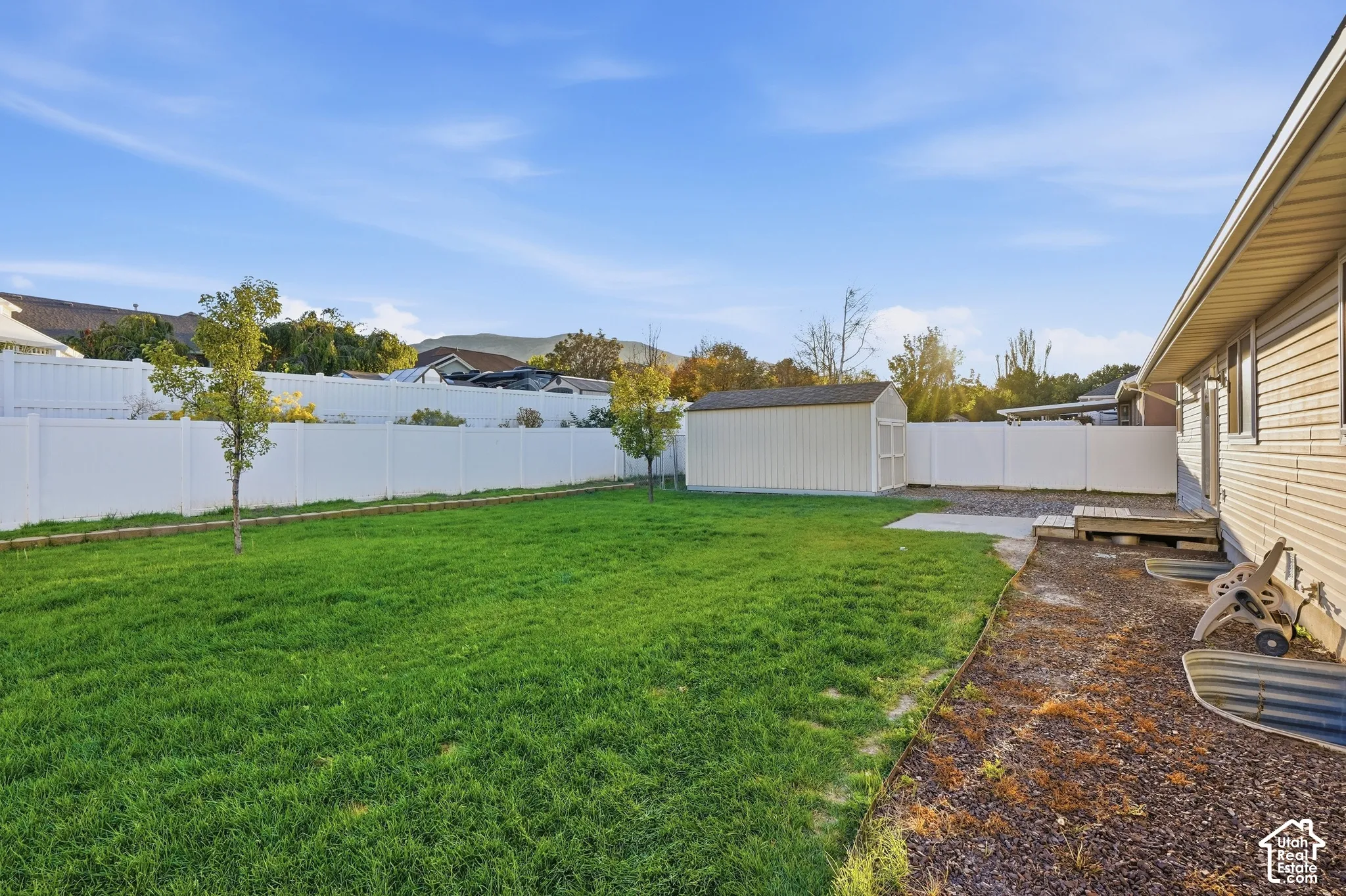 Expansive grassy yard with a white privacy fence and a detached storage shed