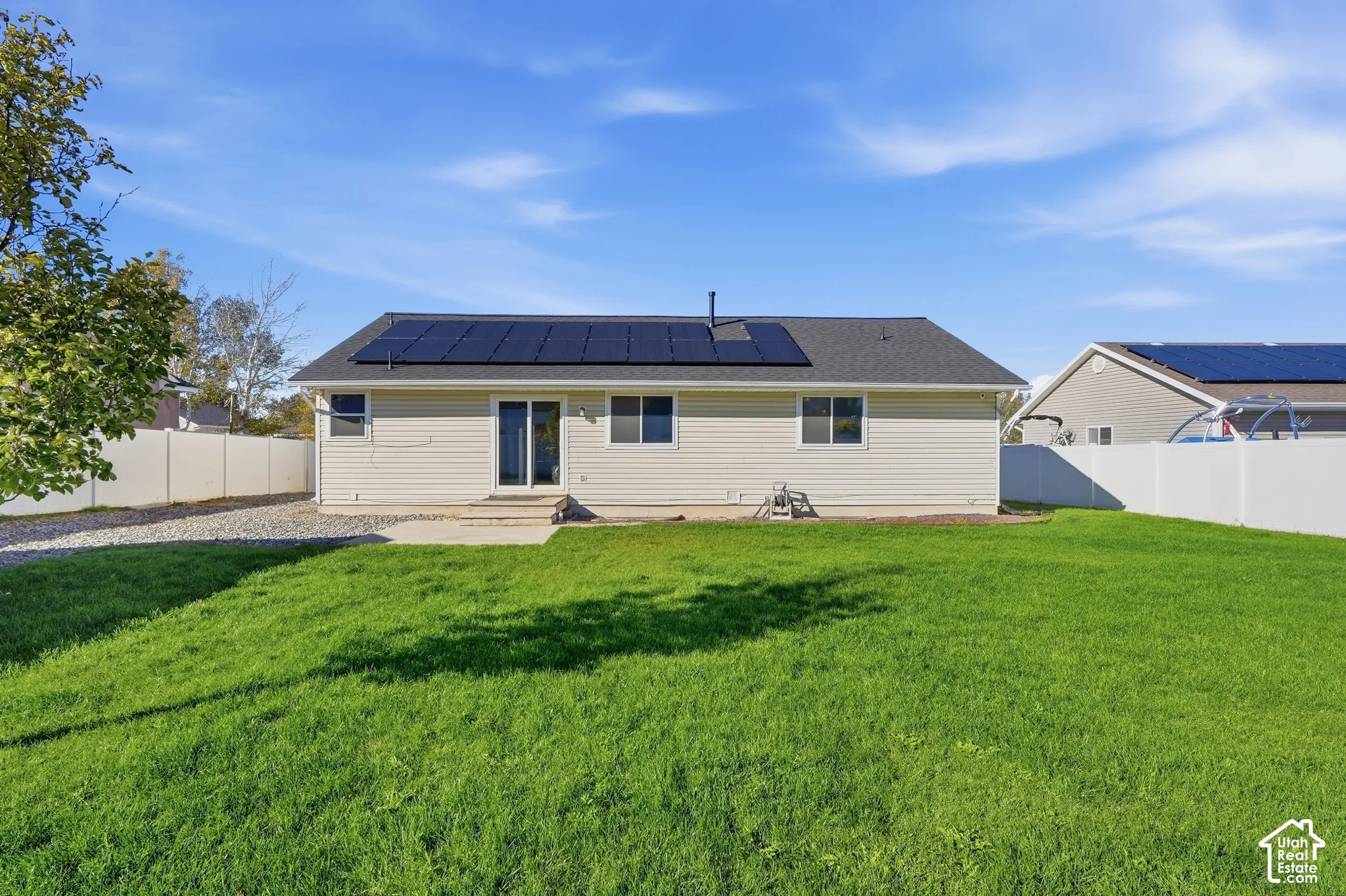 Expansive backyard featuring a green lawn, concrete patio, and full vinyl fencing