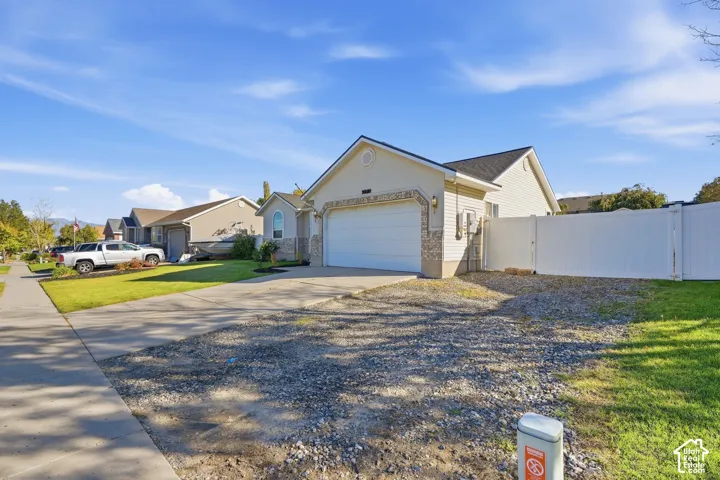 Single-story residence featuring a two-car garage, stone facade accents, and a white privacy fence