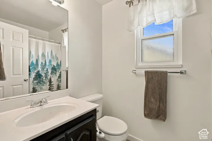 Vanity with white countertop, chrome faucet, wall-mounted mirror, white window frame, and toilet