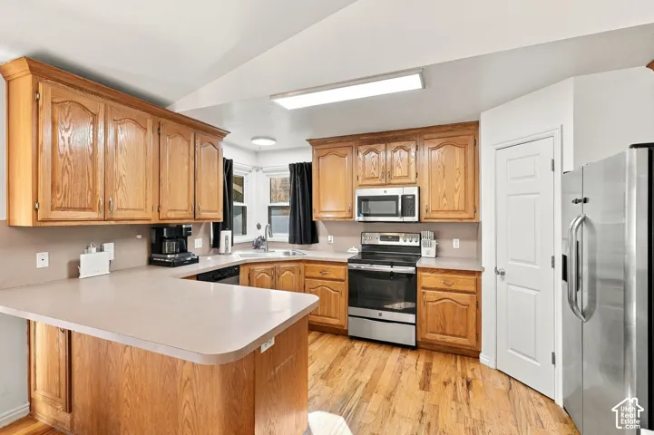 Well-appointed kitchen featuring wood cabinetry, stainless steel appliances, a breakfast bar, and wood-finish flooring