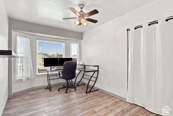 Bay window with blinds, wood-finish flooring, and ceiling fan with integrated lighting