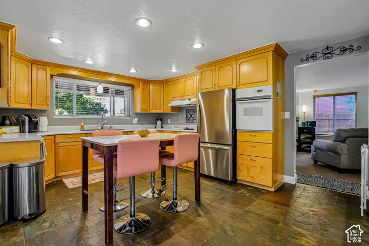 Kitchen featuring wood cabinetry, stainless steel appliances, stone-look flooring, recessed lighting, and a built-in oven