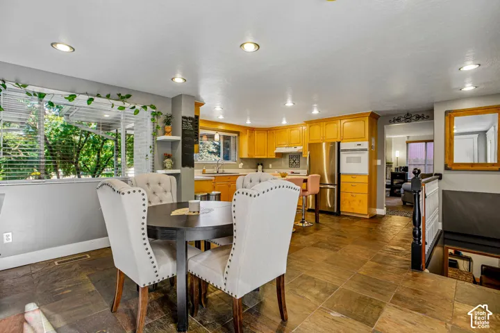 Kitchen and dining area featuring stone tile flooring, recessed lighting, wood cabinetry, and stainless steel appliances