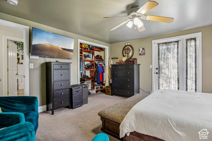 Carpeted bedroom with a ceiling fan, French doors, and built-in closet organization