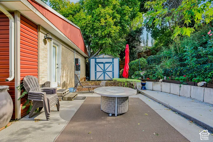 Concrete patio with a woven-look fire pit, red siding, and a white storage shed