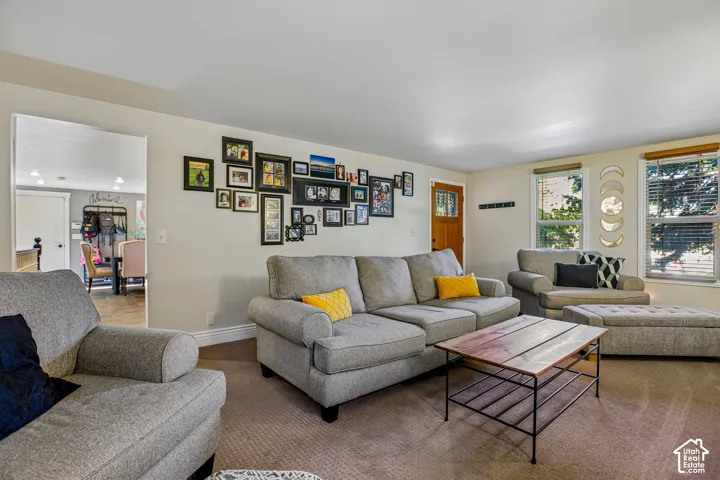 Carpeted living area with light-toned walls, multiple windows, and a wood-finish entry door