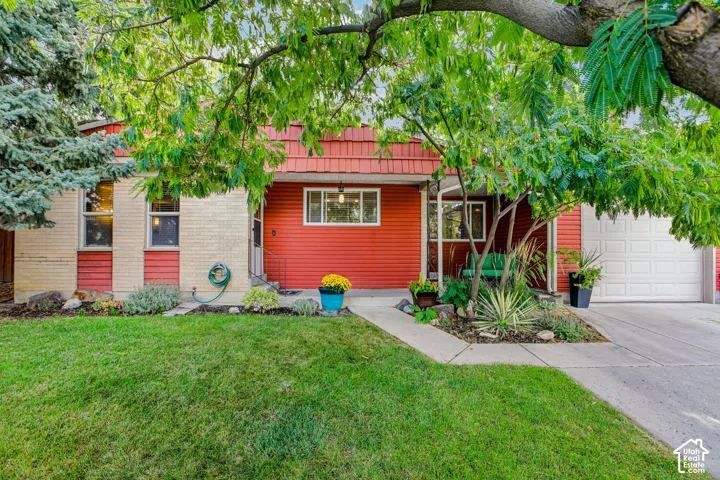 Red siding exterior with brick accents, attached garage, concrete driveway, and front landscaping