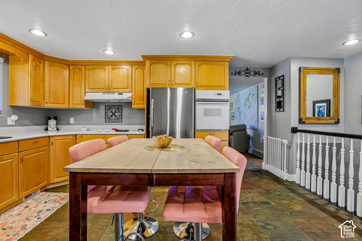 Kitchen featuring warm wood cabinetry, stainless steel appliances, recessed lighting, and stone-finish flooring