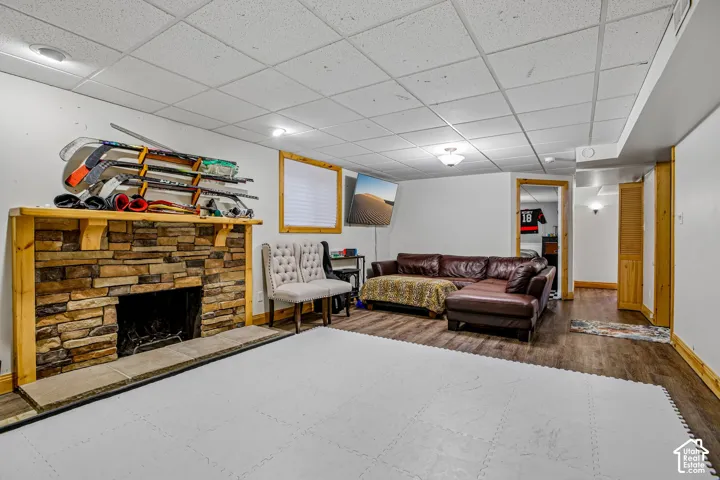 Spacious room featuring a stone-clad fireplace with wood mantle, drop ceiling, recessed lighting, and wood-finish flooring