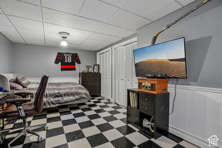 Black and white checkered flooring, white paneled lower walls, gray upper walls, white bi-fold closet doors, and a suspended acoustic tile ceiling