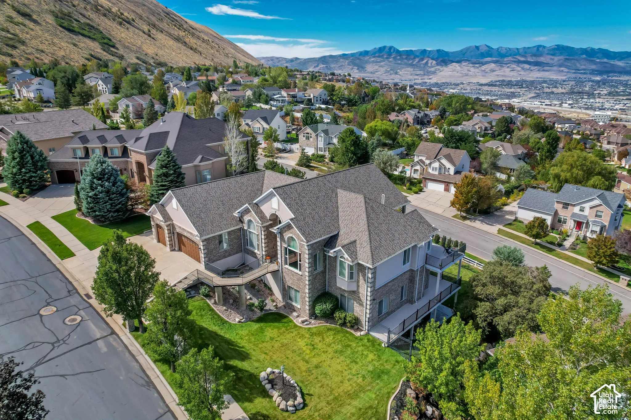 Multi-level residence featuring a prominent gabled roofline, stone and siding exterior, two attached garages, a two-story bay window, and extensive decking
