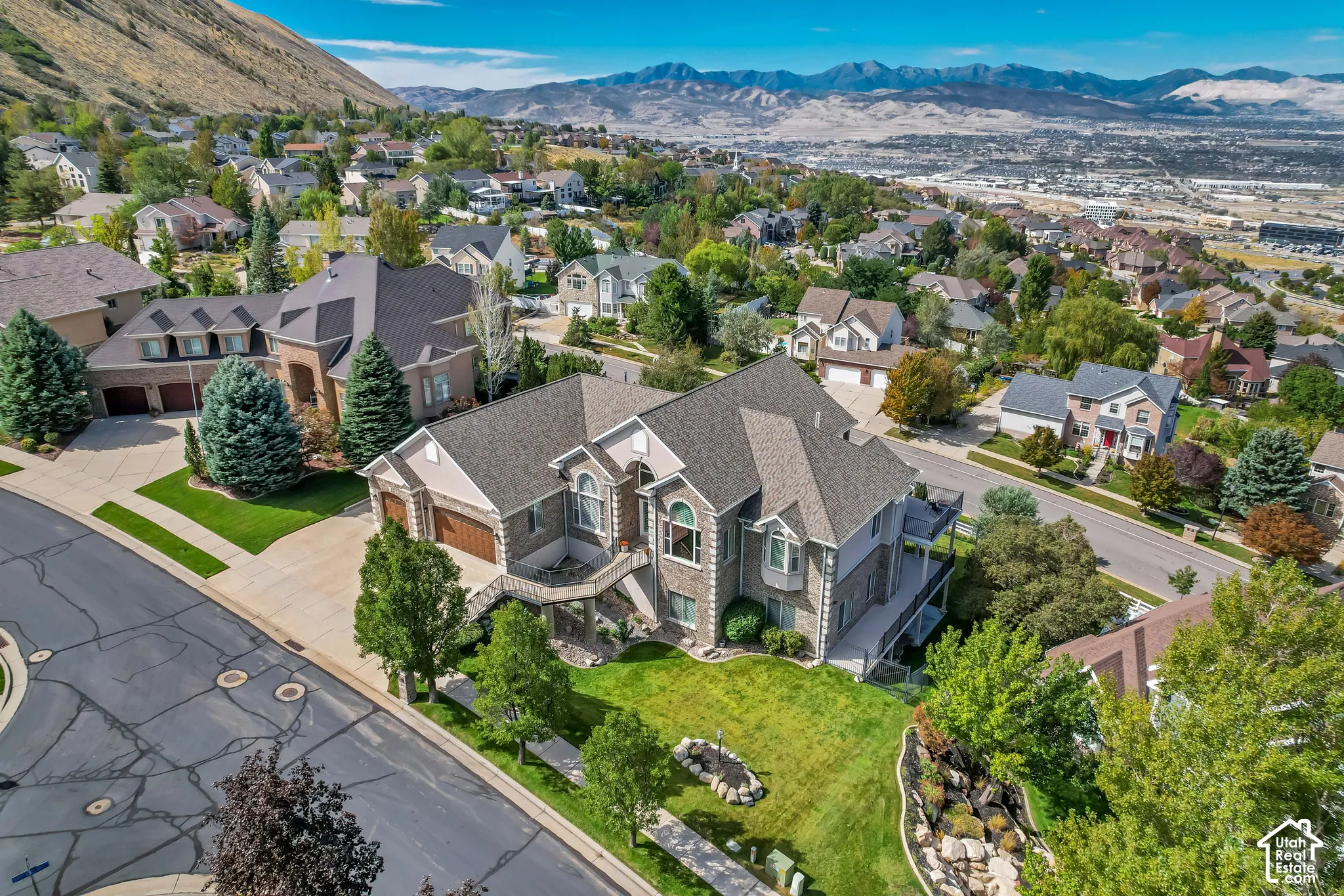 Two-story residential exterior with a stone and siding facade, featuring a prominent bay window, attached two-car garage, and a spacious front lawn with mature landscaping