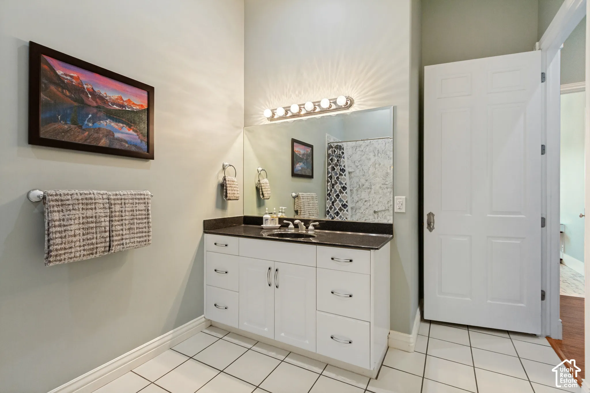 White shaker vanity with dark countertop, large vanity mirror, and polished chrome light fixture