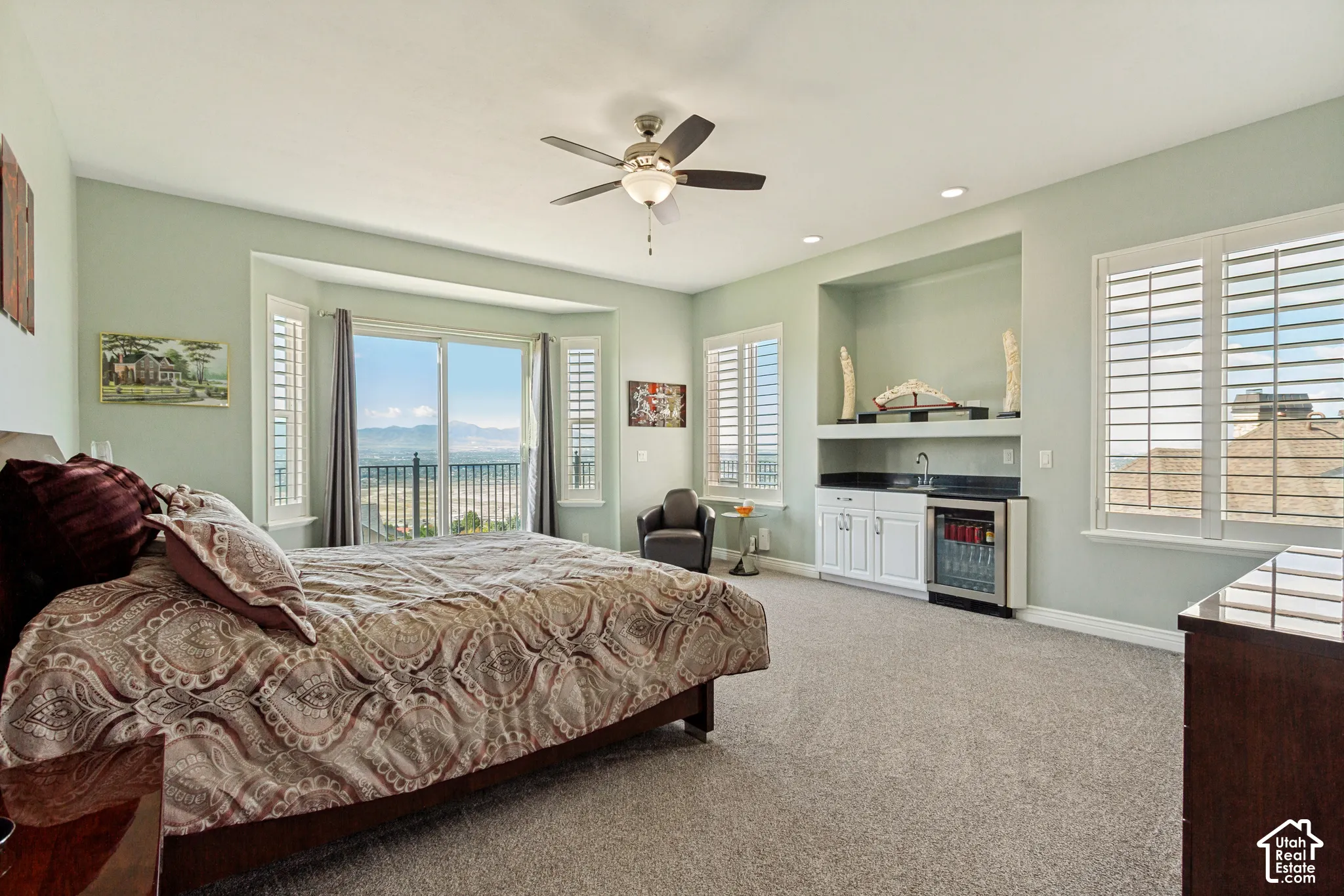 Sliding glass doors with a balcony, multiple windows with plantation shutters, ceiling fan, recessed lighting, and a built-in wet bar with cabinetry