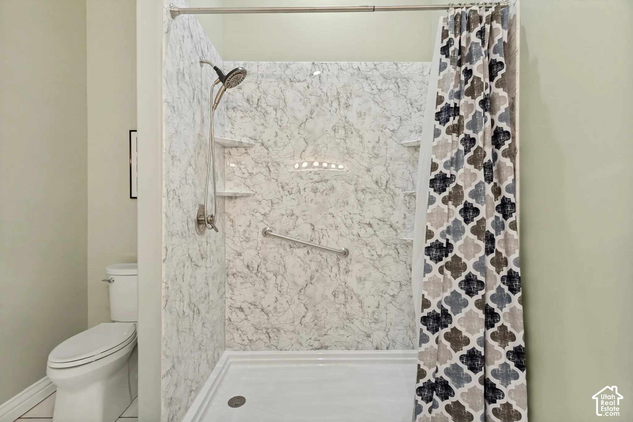 Shower with marble-patterned wall panels, integrated shelving, and a grab bar
