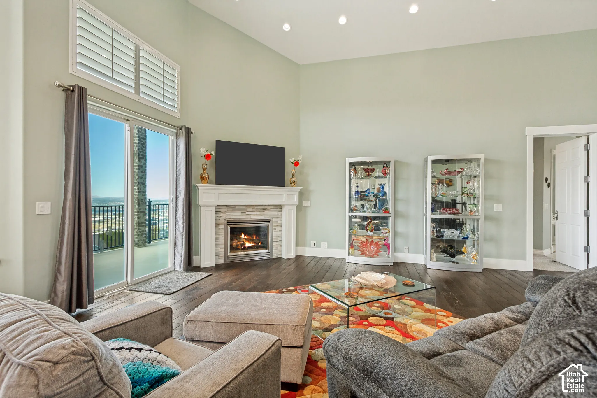 Vaulted ceiling living area featuring a stone-surround fireplace with a white mantel, wood-finish flooring, and sliding glass doors to an exterior balcony