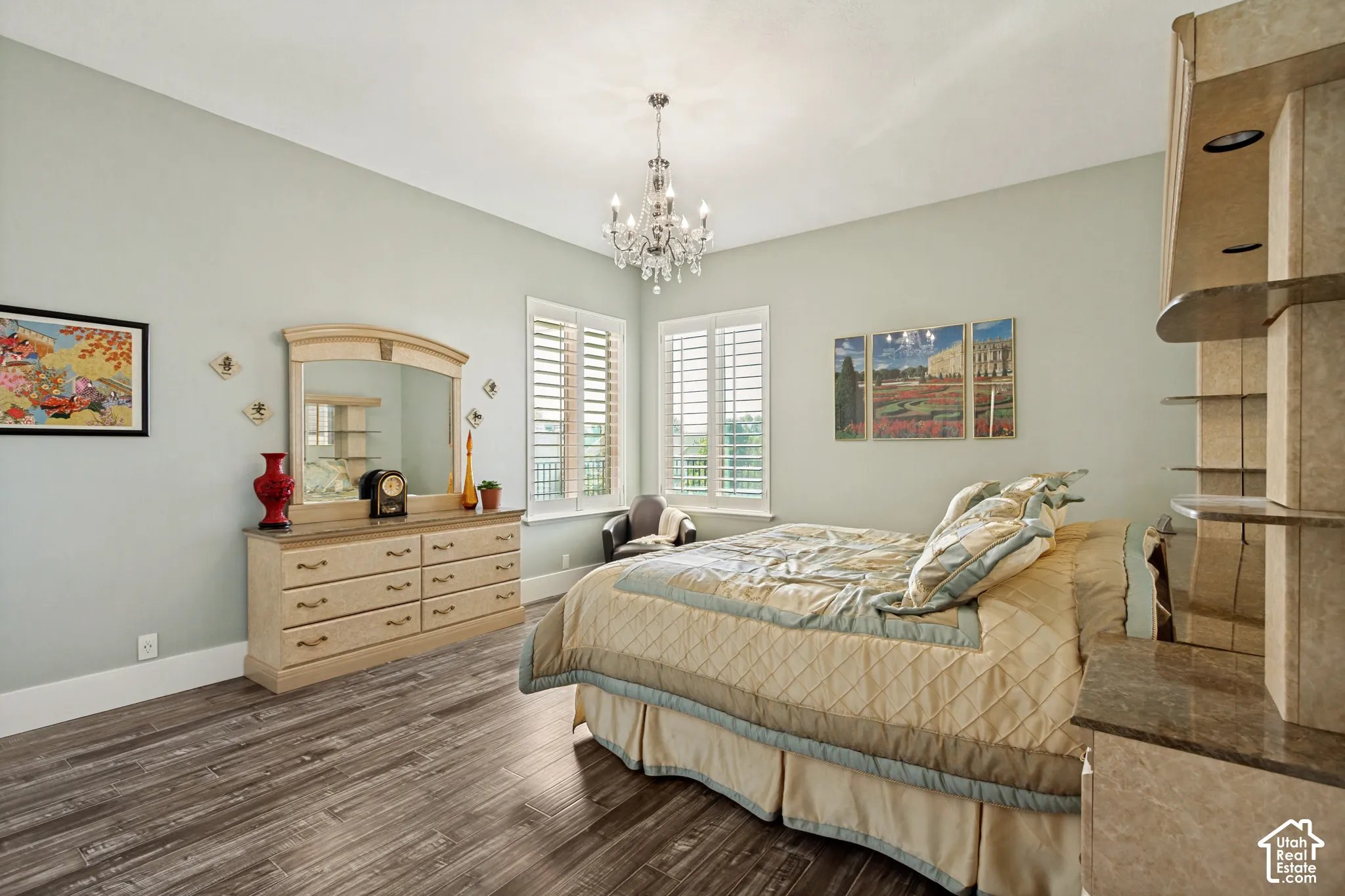 Spacious primary bedroom featuring soft sage-green walls, wood-finish flooring, and abundant natural light from dual shuttered windows