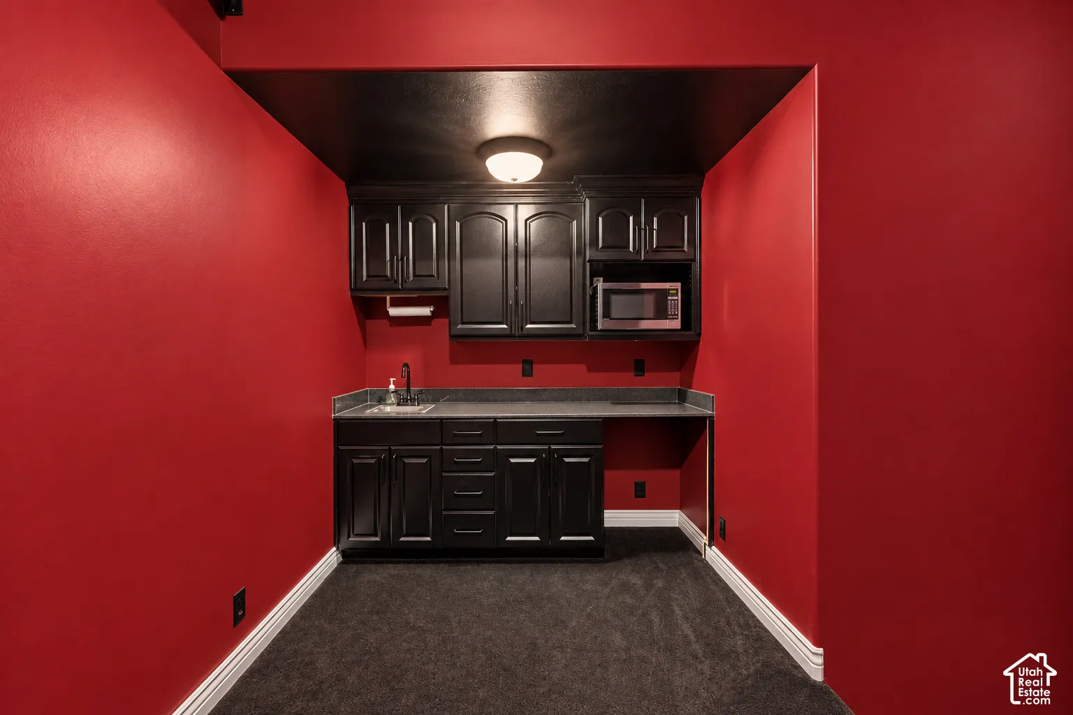 Wet bar featuring dark cabinetry, a countertop, an undermount sink with a faucet, and an integrated microwave