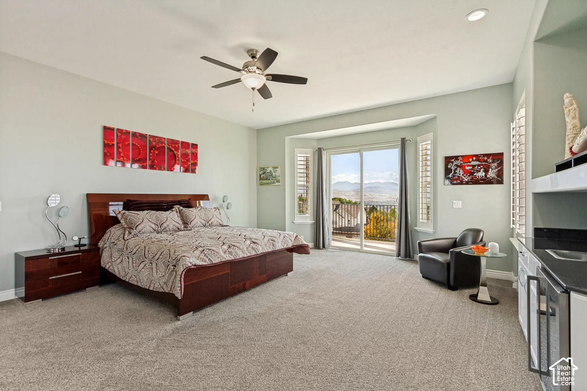 Expansive bedroom featuring carpet flooring, a ceiling fan, a built-in wet bar with a compact refrigerator, and sliding glass doors to an exterior balcony