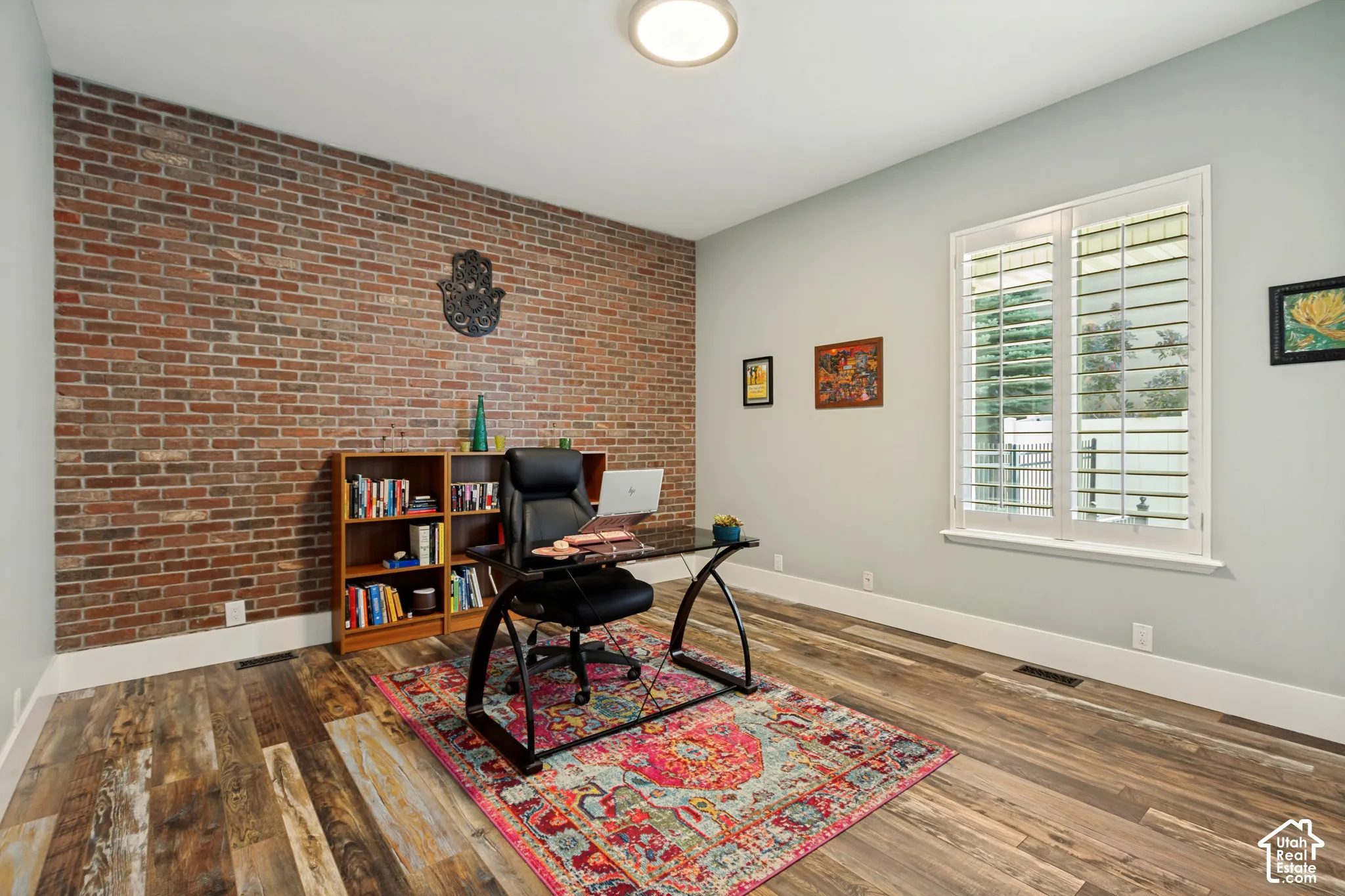 Exposed brick wall, wood-finish flooring, recessed lighting, and a window with plantation shutters