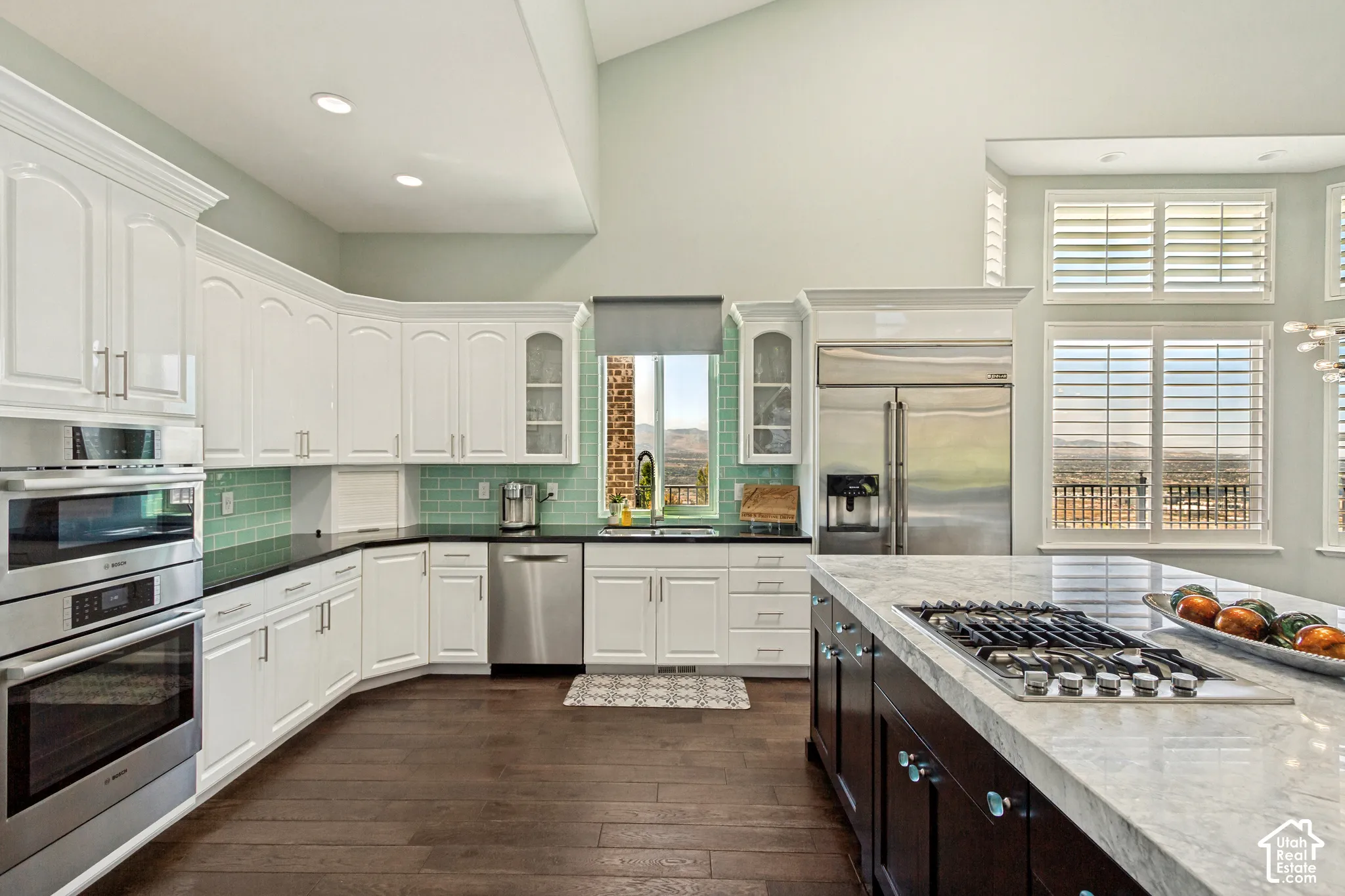 Well-appointed kitchen featuring white cabinetry, stainless steel appliances, a tiled backsplash, wood-finish flooring, and a central island with a cooktop