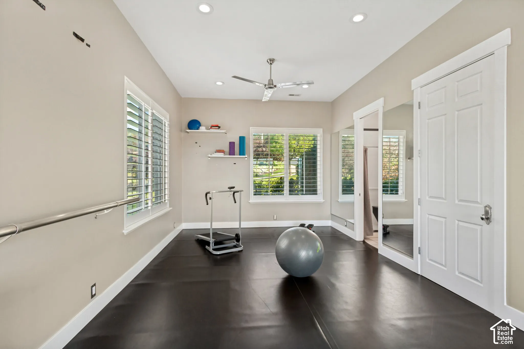 Spacious room with dark flooring, multiple windows featuring plantation shutters, recessed lighting, and a ceiling fan