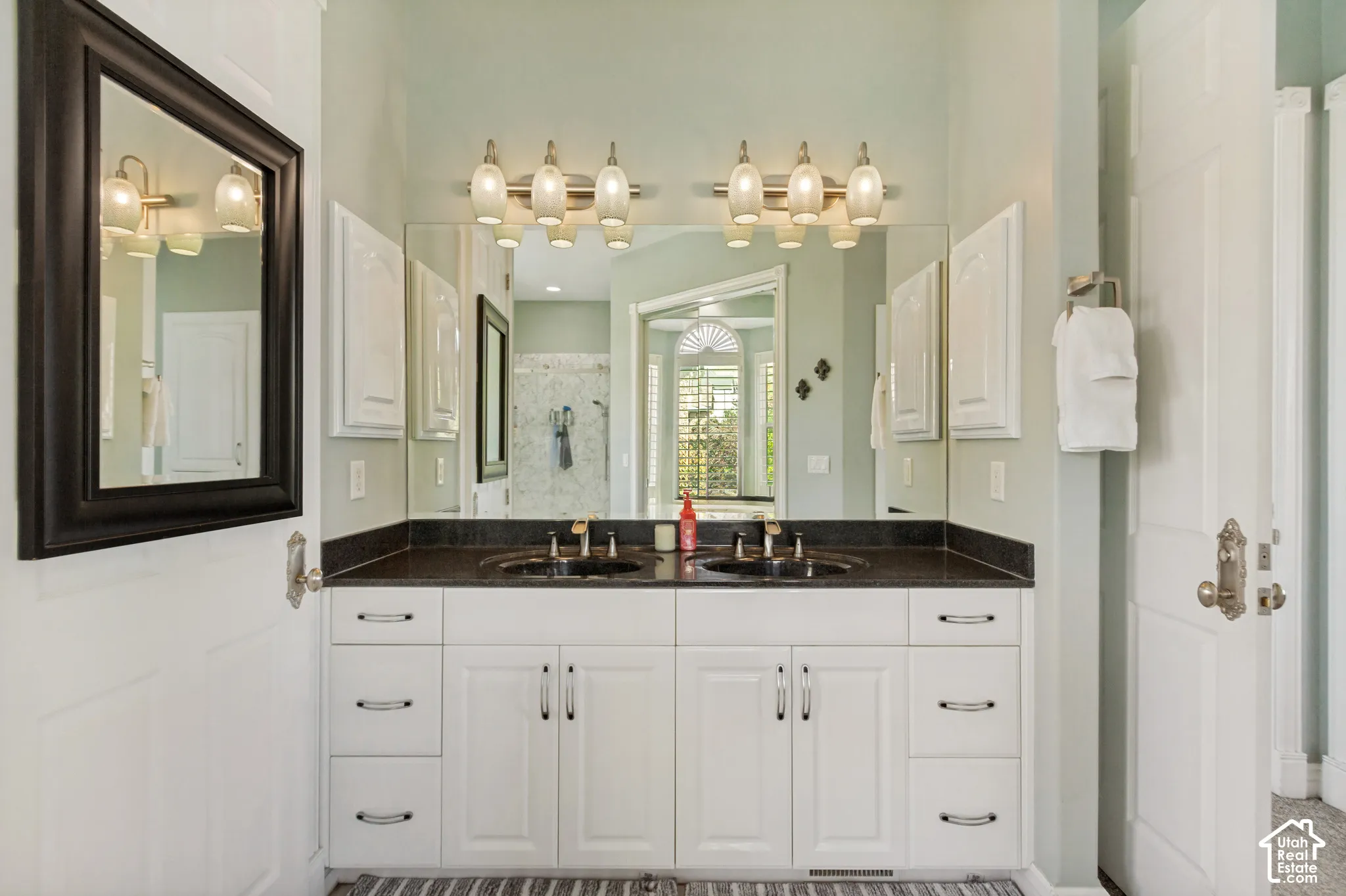 Double vanity with undermount sinks, black countertop, white cabinetry, and wall-mounted light fixtures