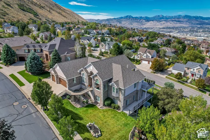 Multi-level residence featuring a prominent gabled roofline, stone and siding exterior, two attached garages, a two-story bay window, and extensive decking