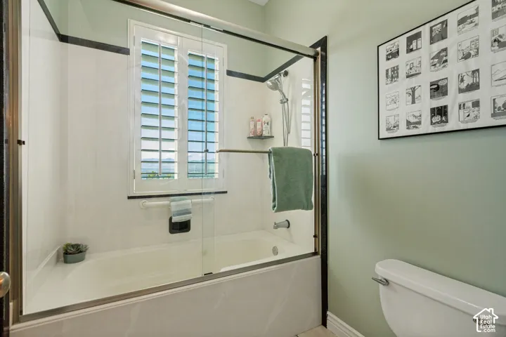 Bathtub and shower combination with a clear glass enclosure, white plantation shutters, and a white tile surround