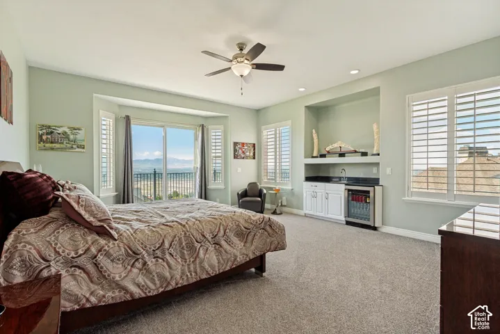 Sliding glass doors with a balcony, multiple windows with plantation shutters, ceiling fan, recessed lighting, and a built-in wet bar with cabinetry