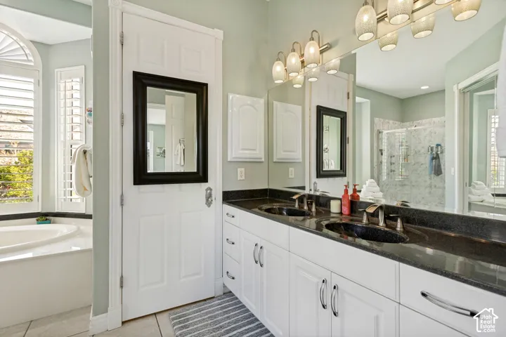 Dual vanity with dark countertop and undermount sinks, white cabinetry with chrome hardware, full-width mirror, and multi-bulb light fixture