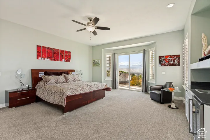 Expansive bedroom featuring carpet flooring, a ceiling fan, a built-in wet bar with a compact refrigerator, and sliding glass doors to an exterior balcony