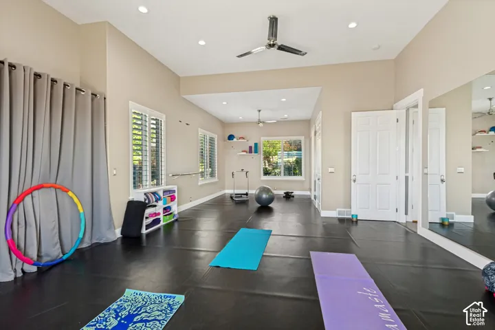 Spacious room featuring dark flooring, multiple windows with plantation shutters, ceiling fans, recessed lighting, and wall-mounted mirrors