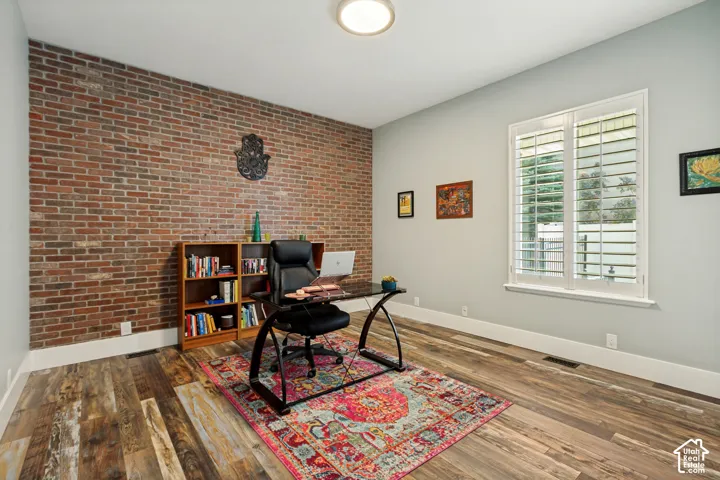 Exposed brick wall, wood-finish flooring, recessed lighting, and a window with plantation shutters