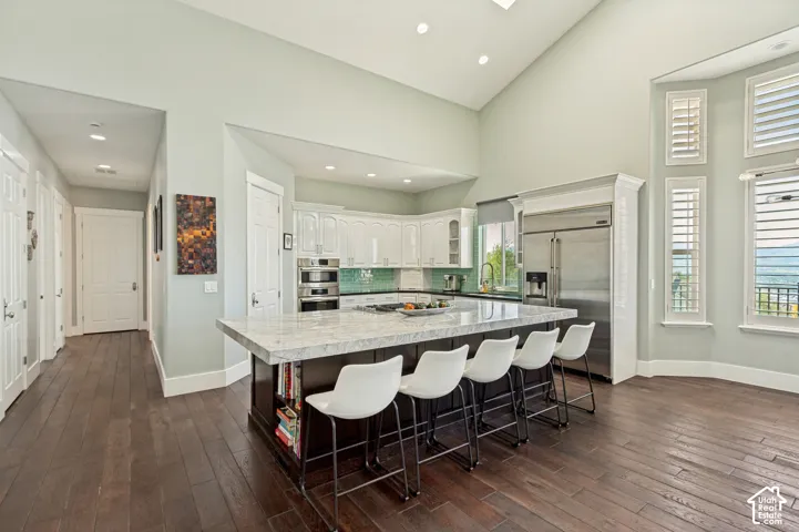 Vaulted ceiling, wood-finish flooring, central island with seating, stainless steel appliances, and plantation shutters