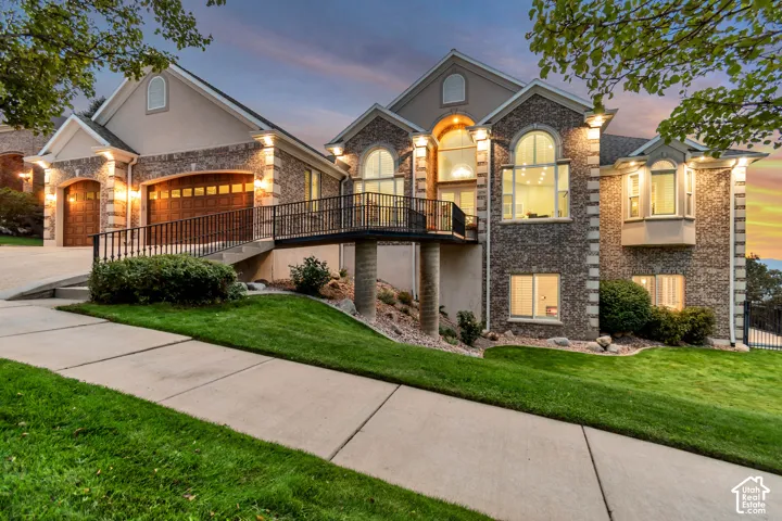 Multi-level residence featuring a brick and stucco exterior, arched windows, a two-car garage with wood-finish doors, and a pedestrian ramp leading to an upper-level entrance