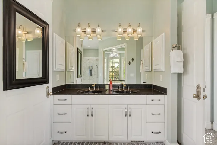 Double vanity with undermount sinks, black countertop, white cabinetry, and wall-mounted light fixtures