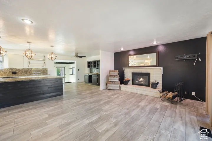 Open-concept living area featuring wood-finish flooring, a brick-surround fireplace, recessed lighting, and a kitchen island with pendant lighting
