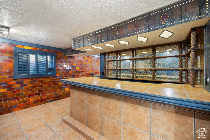 Commercial-style counter service area featuring warm wood-finish countertop, blue-trimmed glass display cases with interior shelving, vibrant hand-laid tile backsplash in orange and red tones, and recessed lighting throughout