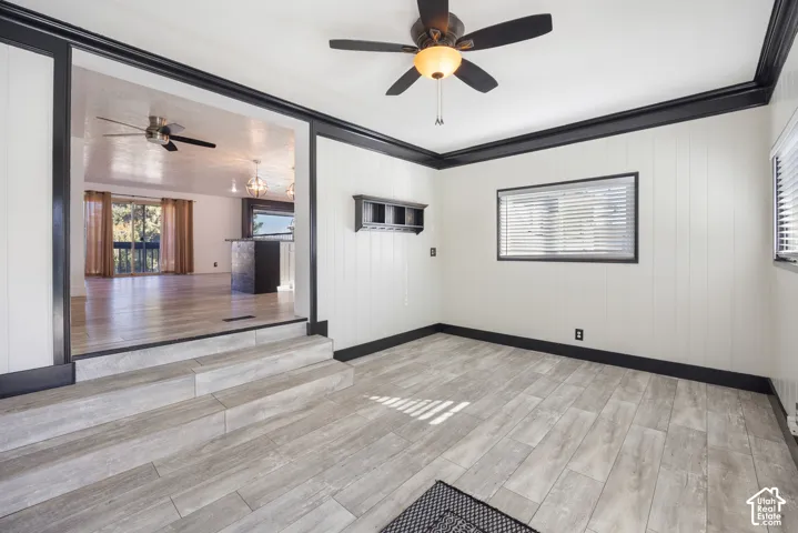 Bright, open room featuring wood-finish flooring, ceiling fan with integrated lighting, and large windows providing natural light