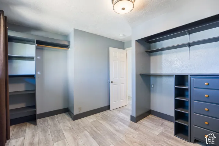 Spacious walk-in closet featuring dual clothing rods with multiple shelving sections, wood-finish flooring, recessed ceiling lighting, and abundant storage with built-in cabinetry including a multi-drawer dresser unit