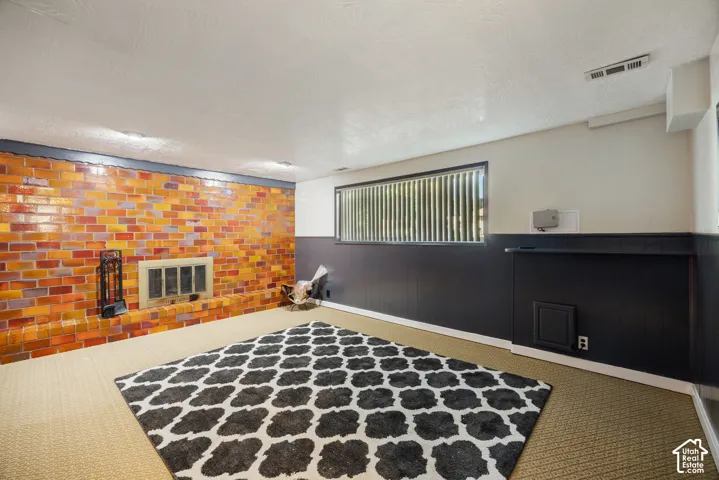 Finished basement featuring exposed brick accent wall with warm orange and charcoal tones, polished concrete flooring, and dark wainscoting