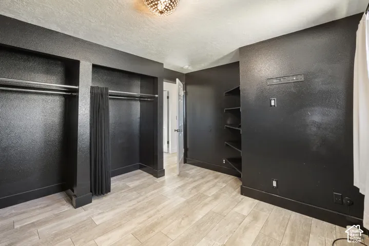 Spacious walk-in closet featuring dual clothing rods with curtain dividers, wood-finish flooring, recessed shelving along accent walls, and abundant natural storage capacity
