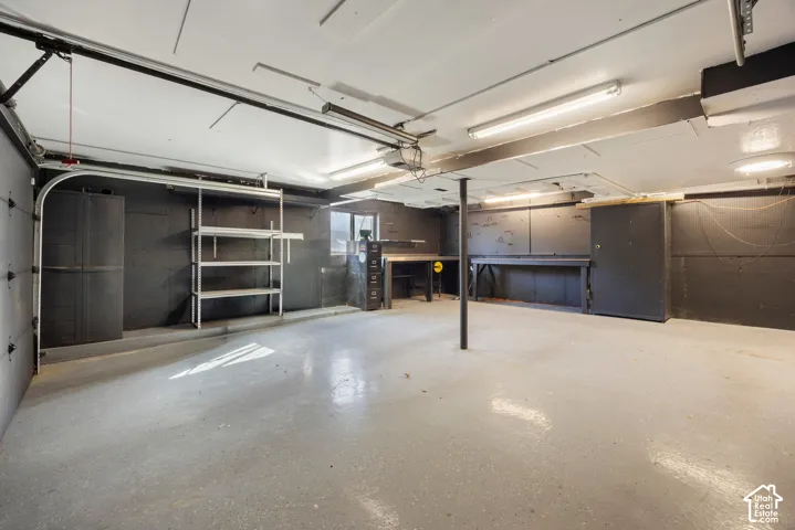 Spacious garage featuring polished concrete flooring, overhead lighting, sectional garage doors with windows, and built-in wall-mounted shelving for storage and organization