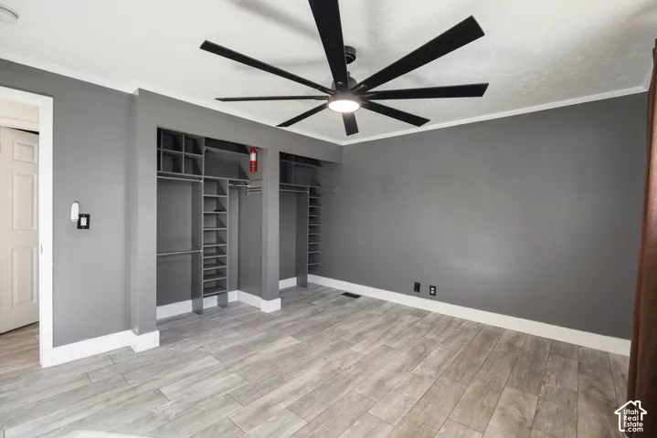 Spacious room featuring wood-finish flooring, two built-in closet systems with shelving and hanging rods, a modern ceiling fan with integrated lighting, and white crown molding
