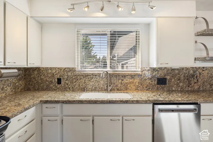 Modern kitchen featuring white cabinetry, speckled granite countertops, stainless steel appliances including a dishwasher, and a deep undermount sink with chrome faucet